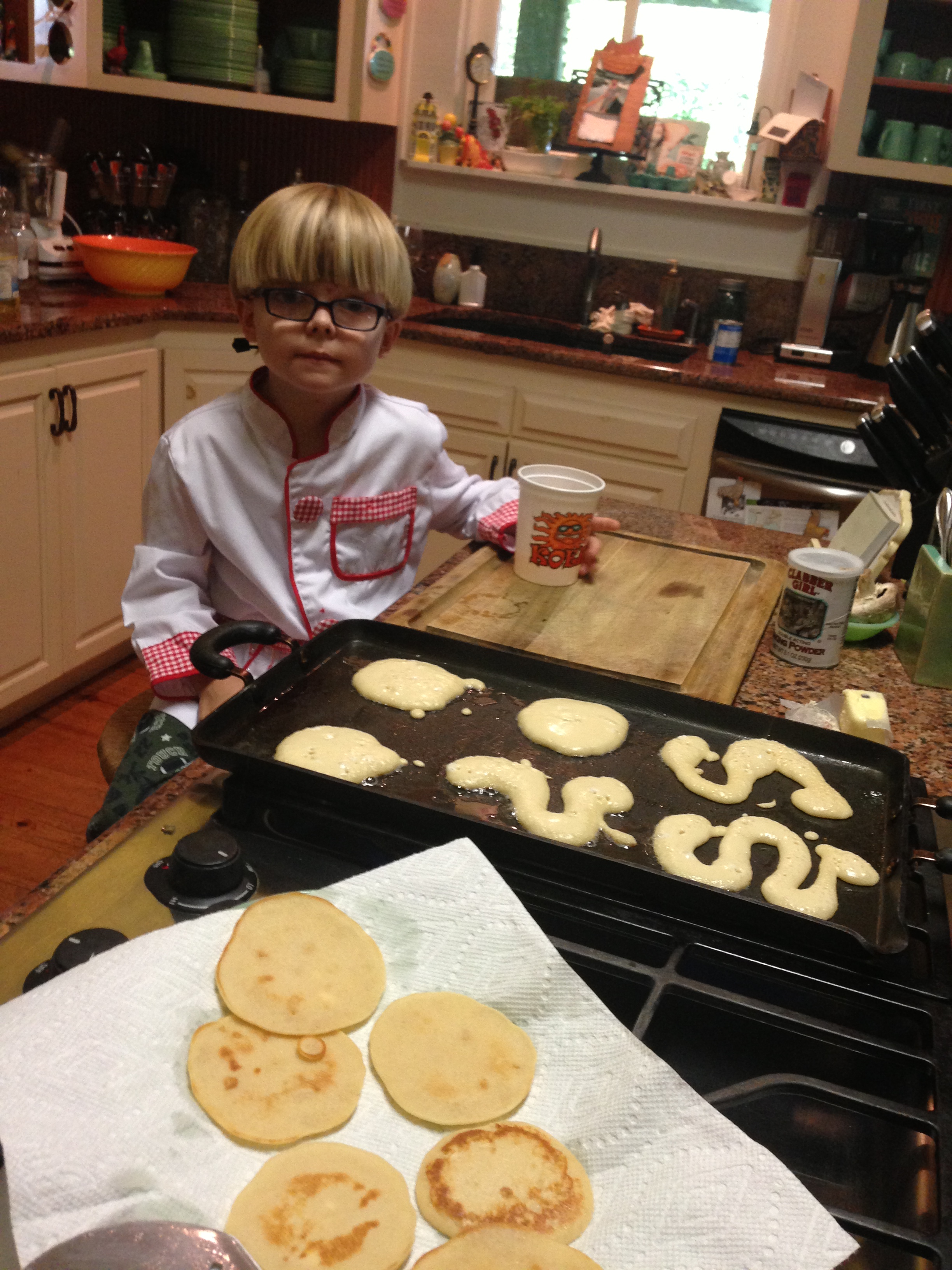 Adorable little chef in kitchen assisting with making pancakes