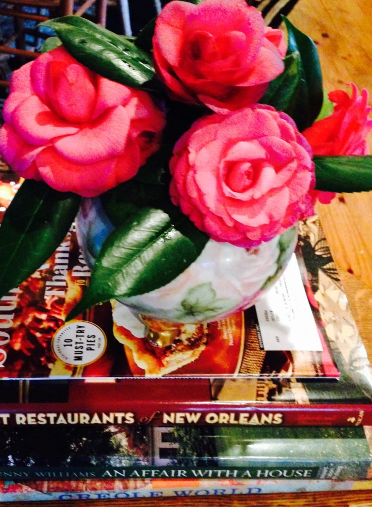 Pink camellia's in hand painted vase sitting on top Books about New Orleans