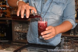 Bartender in denim shirt pouring a burgundy cocktail before going to Hip Fairhope Outdoor Event www.diningwithmimi.com
