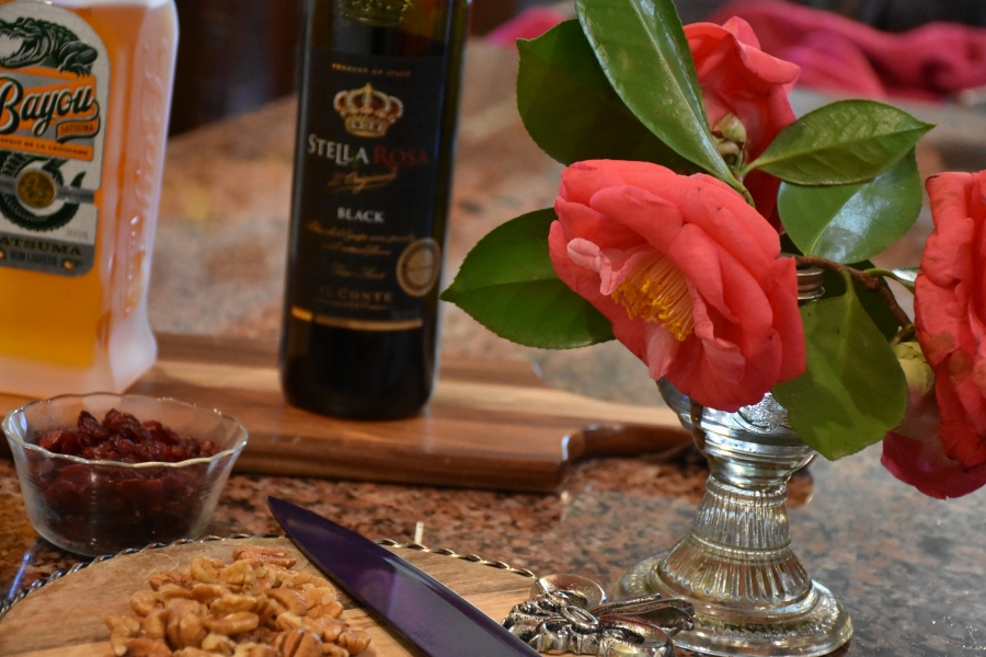 Pecans on cutting board, dried cranberries, Bayou Satsuma Rum, Stella Rossa Black Italian Wine and Large pink Camellias www.diningwithmimi.com